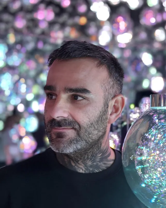 Portrait de Julien Jimenez, expert SEO, barbe poivre et sel, devant un mur de sphères lumineuses aux reflets colorés